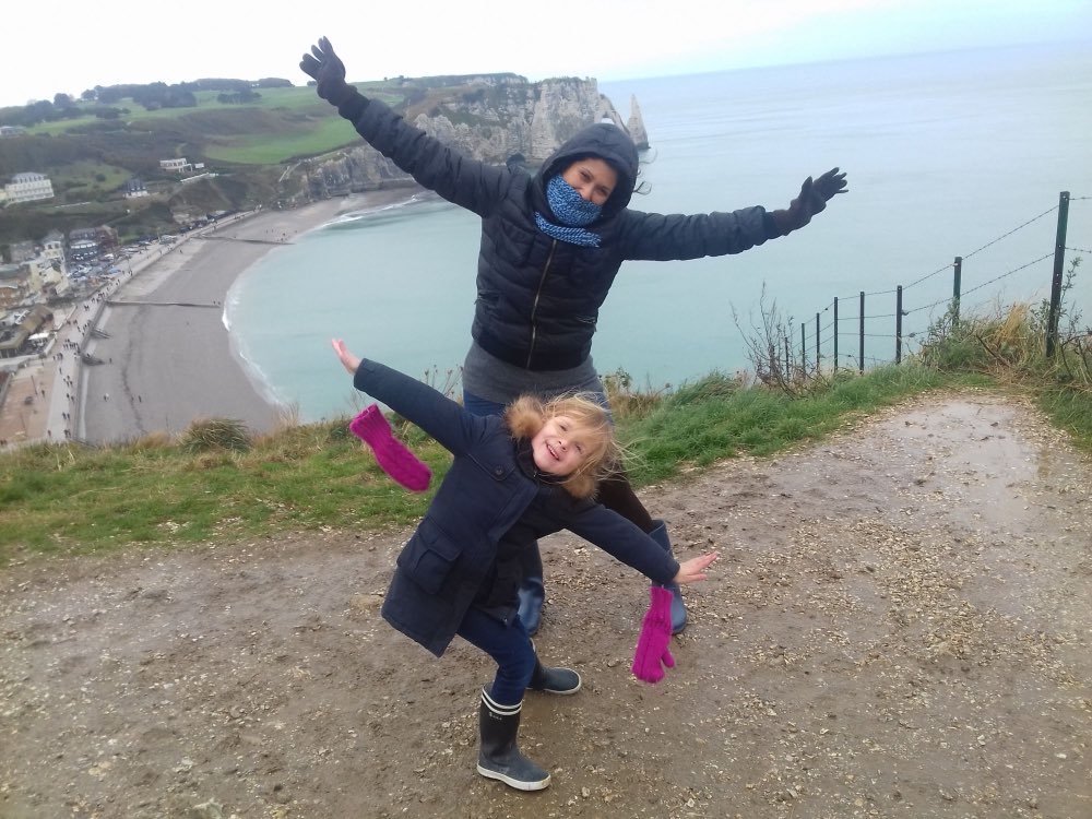 Au pair mexicana y una niña con los brazos abiertos en los acantilados de Étretat, Francia